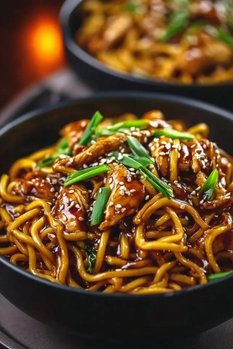 Plate of sticky garlic chicken noodles garnished with green onions.